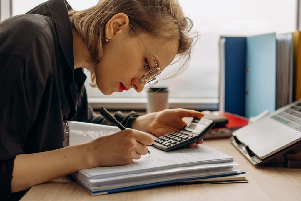 pexels photo 8297034 Young woman diligently working on accounting with a calculator and documents. Perfect for business and finance themes.